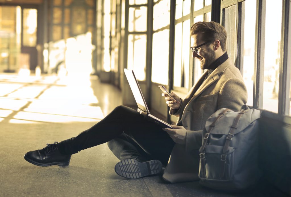 Qriket Review man sitting near window holding phone and laptop