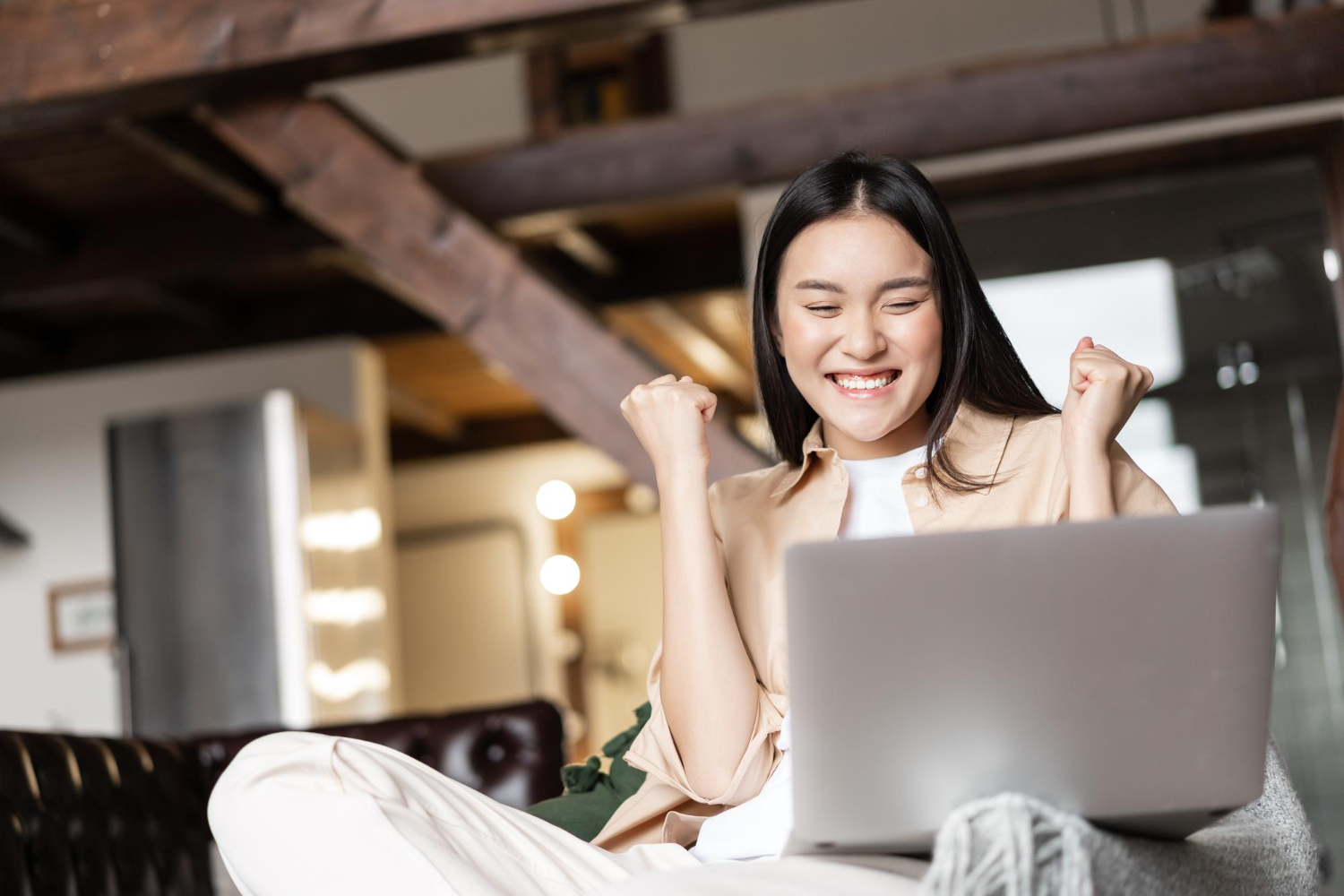 triumphing asian girl winning online celebrating victory while watching video laptop home