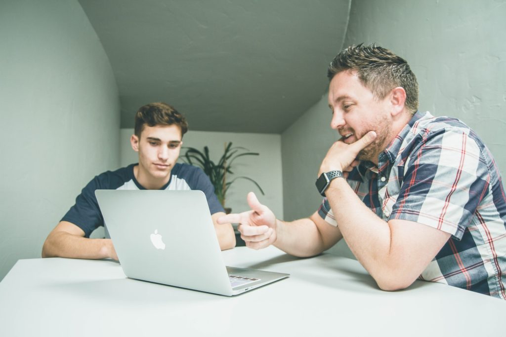 Is Working Solutions A Scam? man wearing white and black plaid button-up sports shirt pointing the silver MacBook